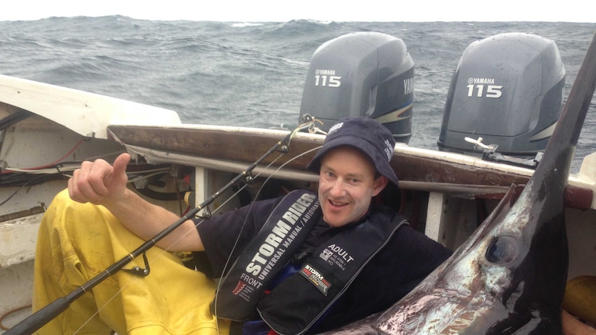 Tasmanian fisherman Leo Miller lies in a boat next to a broadbill swordfish.