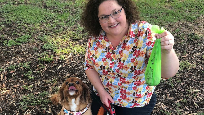 Emily Bryson kneels holding a dog droppings bag with her dog sitting beside her.