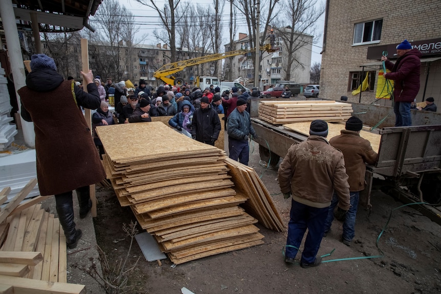 People line up to receive sheets of wood to repair homes damaged in air strikes.