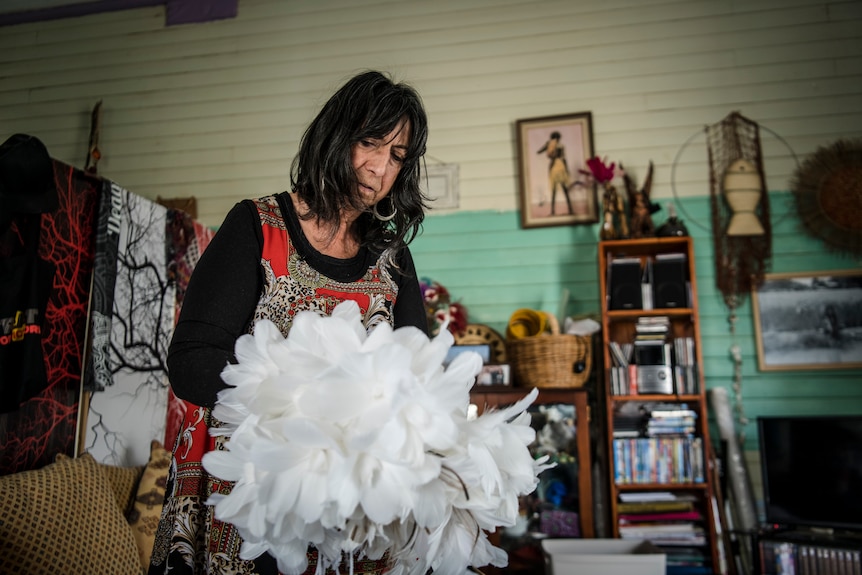 A woman holding a white, flower-like artwork made of feathers.