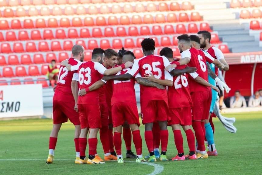 A team of soccer players in red jerseys huddled together, seen from behind.