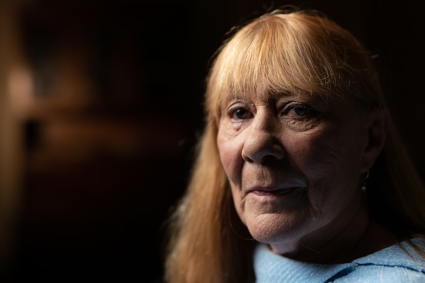 Older woman with blonde hair sitting in a dark room.
