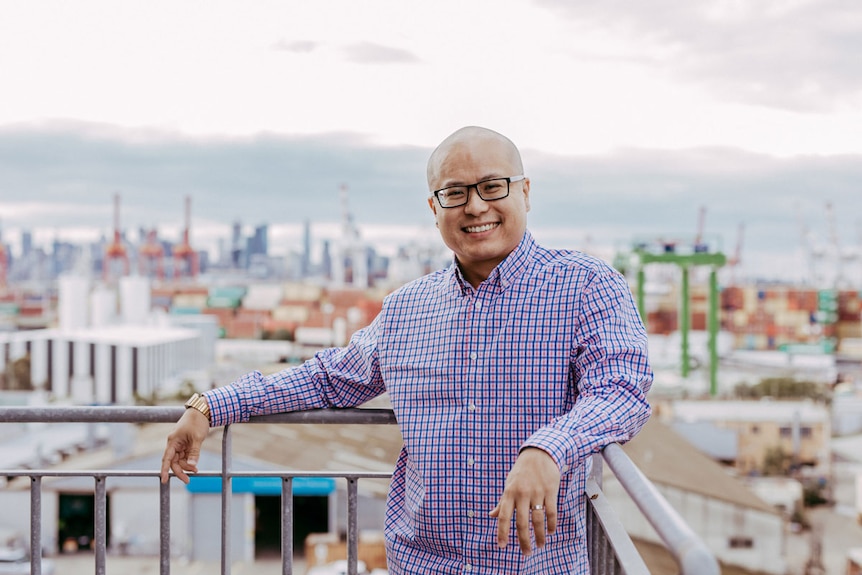 Mortgage broker John Ng stands on a balcony with the suburbs of Melbourne in the background.