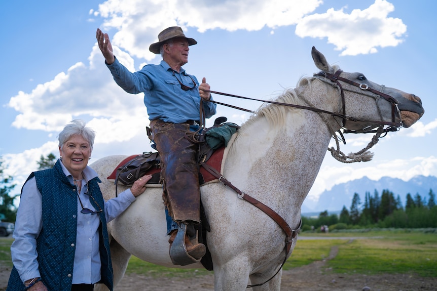 Man sits on horse while woman standing beside them smiles at camera 