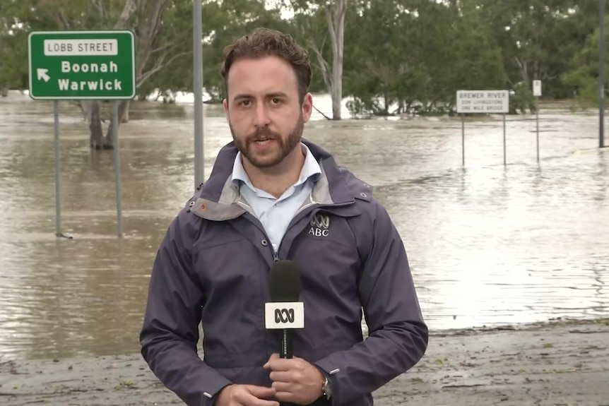 Journalist holding microphone with floods in background.