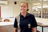 A young school girl wears a navy polo and smiles at camera in classroom