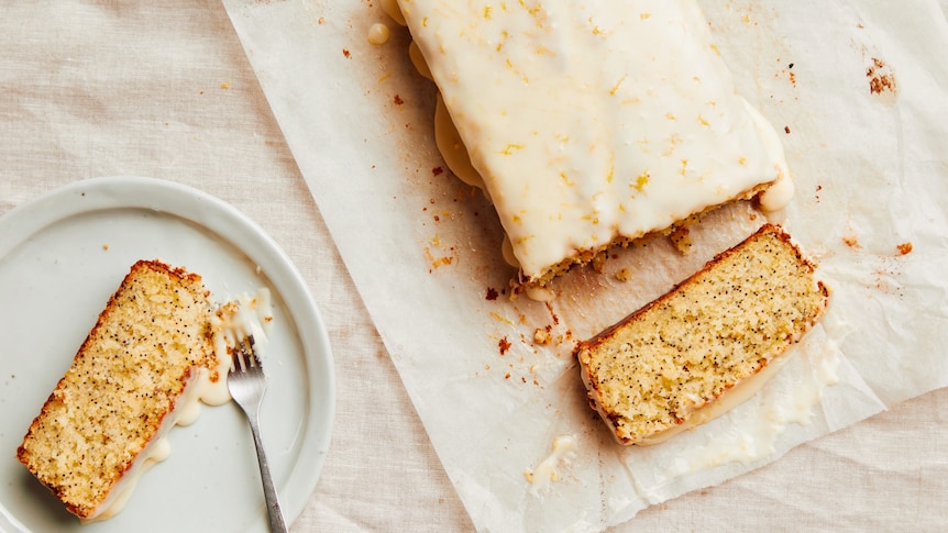 A lemon poppy seed loaf with a sour cream glaze with two slices cut from the cake, a perfect afternoon tea recipe.