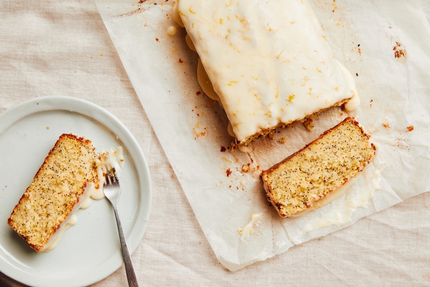 A lemon poppy seed loaf with a sour cream glaze with two slices cut from the cake, a perfect afternoon tea recipe.