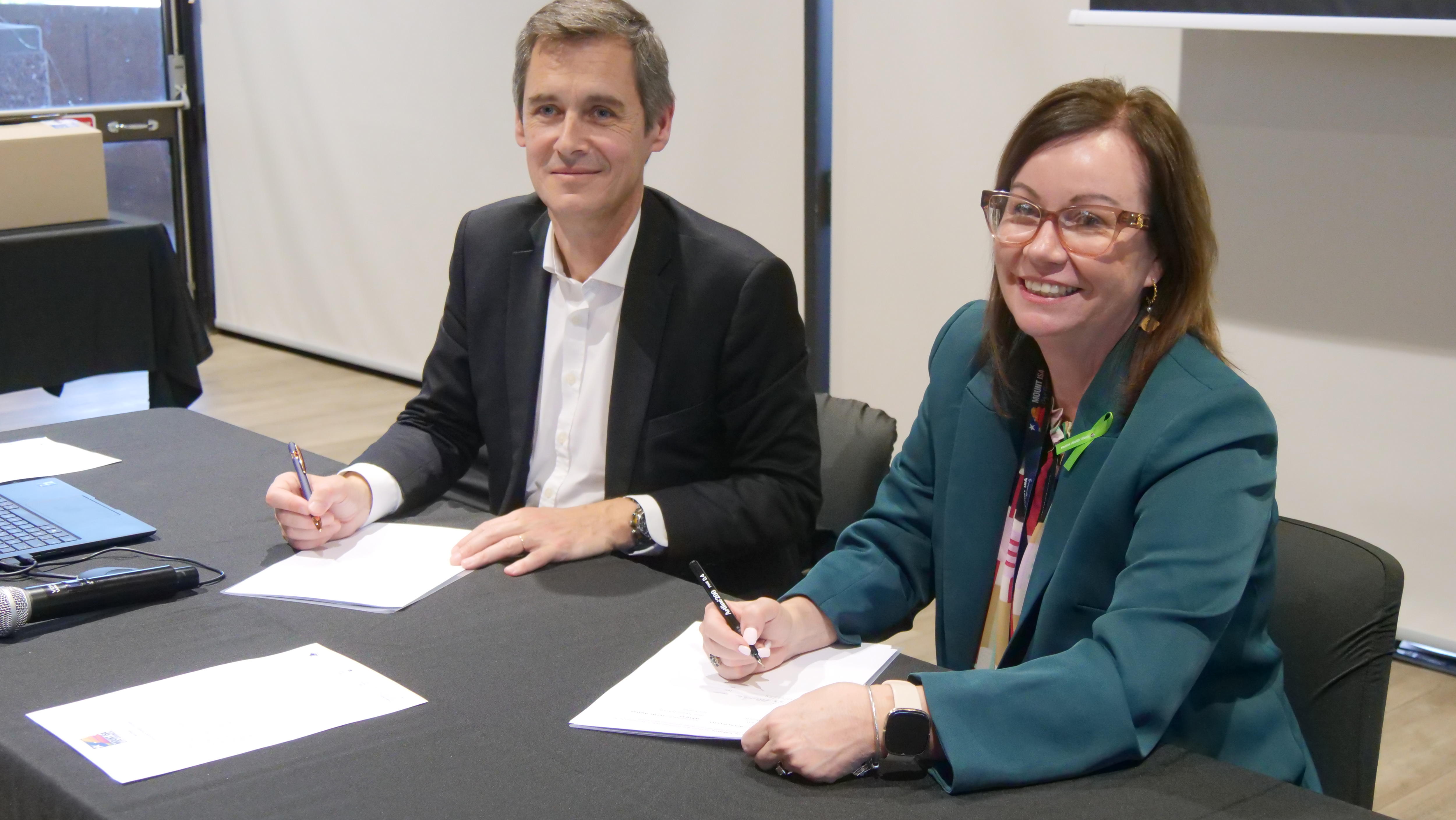 two people sign agreements at a table