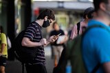 A man looks at his phone with earbuds in, wearing sunglasses and a mask.