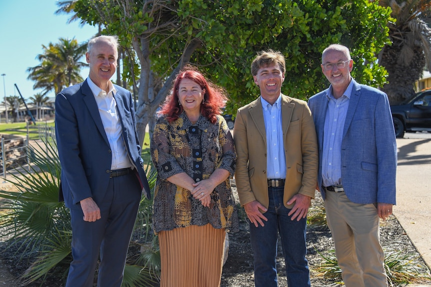 Four people, three men and a woman, stand next to each other smiling at camera at Carnarvon's waterfront