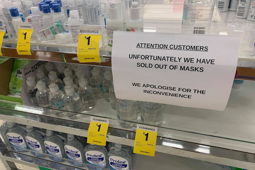 a sign saying "unfortunately we have sold out of masks" is on display in a store, in the hand sanitizer section