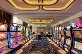 Gaming machines inside Crown Perth's Pearl Room, with gaming tables and casino staff in the background.