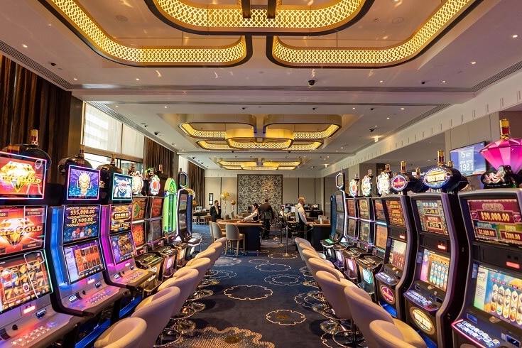 Máquinas de juego dentro de Pearl Room de Crown Perth, con mesas de juego y personal del casino al fondo.