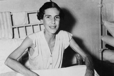 Black and white photo from 1945 of a young nurse very skinny but smiling, sitting up in hospital bed 