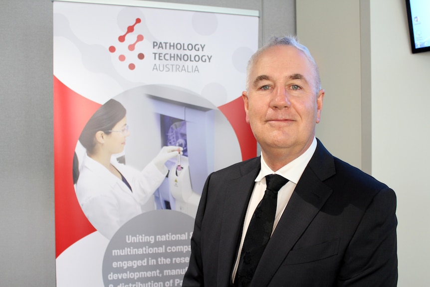 Corporate shot of man in suit standing in front of a Pathology Technology Australia banner.
