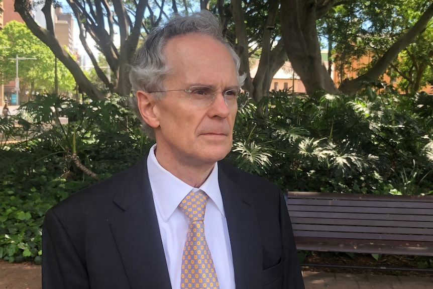 a grey haired man is wearing a suit and staring into the distance 