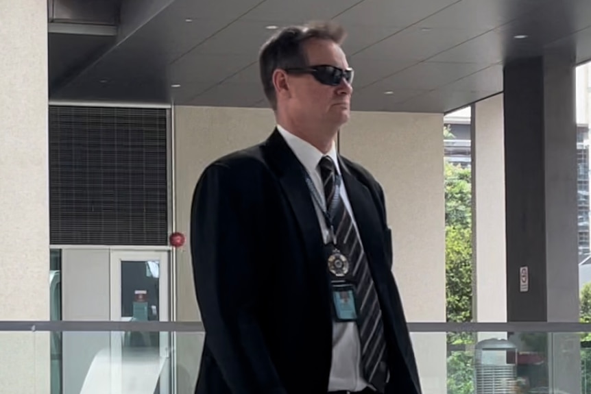 Detective Sergeant Moore walking in a suit with sunglasses