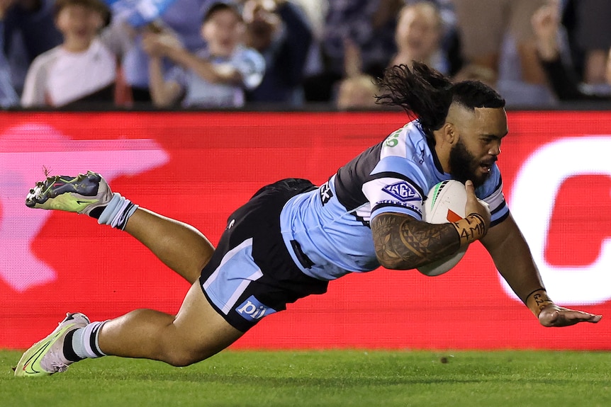 A Cronulla Sharks NRL player holds the ball with his left arm as he dives to score a try.