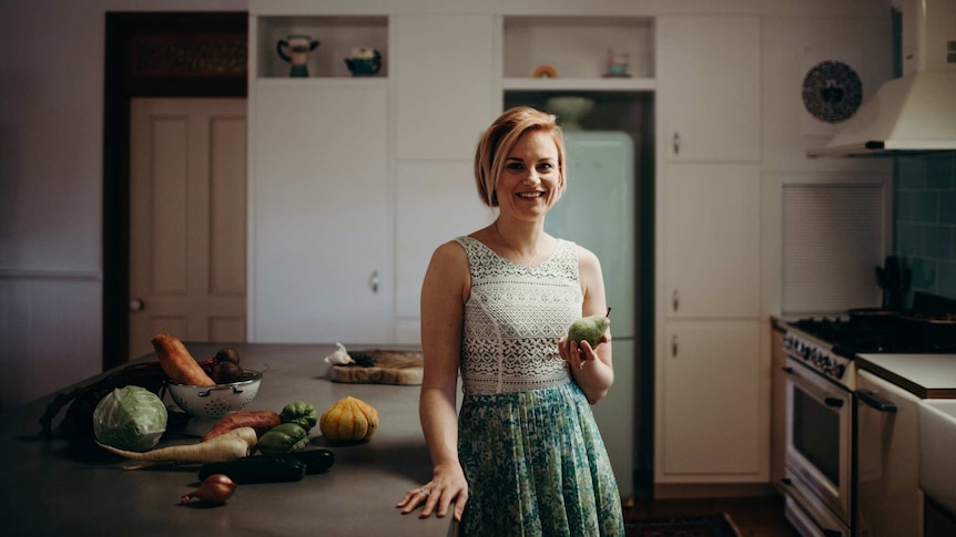 Brisbane based dietitian Emma Blank stands in a home kitchen holding a pear.