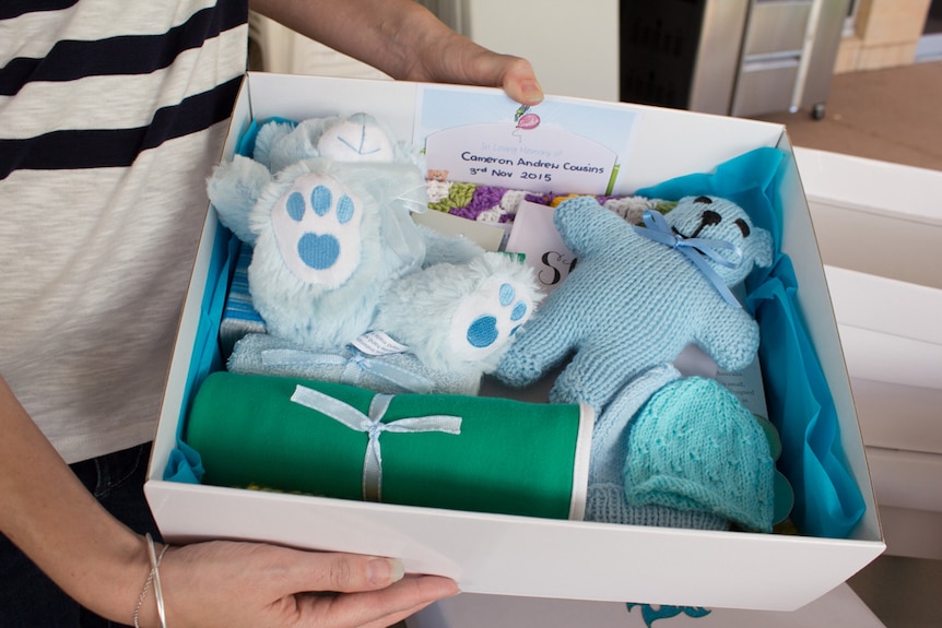 A memory box containing a teddy, woollen hat and wrap.