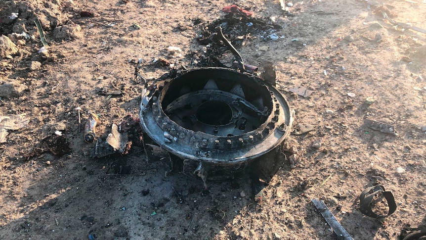 A round plane part is seen on the ground. It is surrounded by debris from the rest of the crash, and sits atop brown dirt.