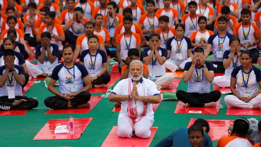 Indian Prime Minister Narendra Modi kneels in a yoga pose with a crowd behind him.