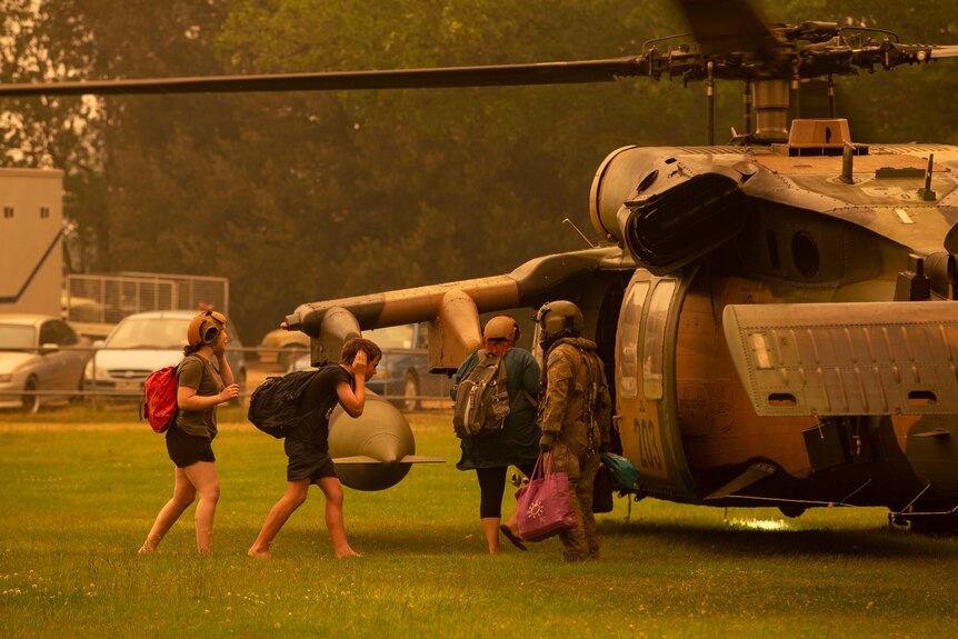 Children cover their ears as they climb aboard a military helicopter.
