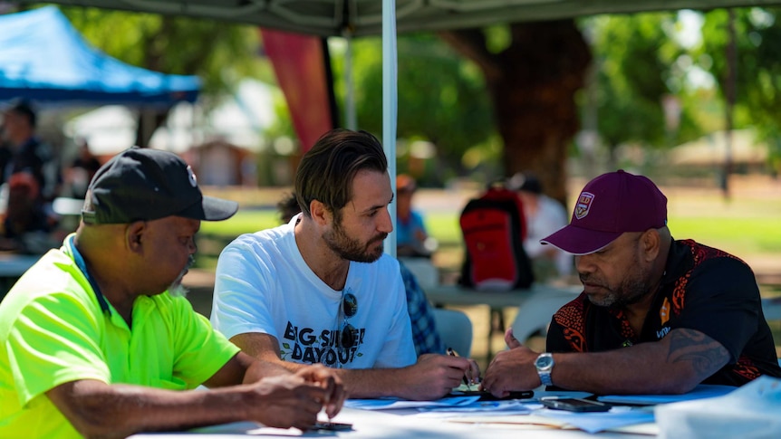 Three men sit around a table in a park in Kununurra.