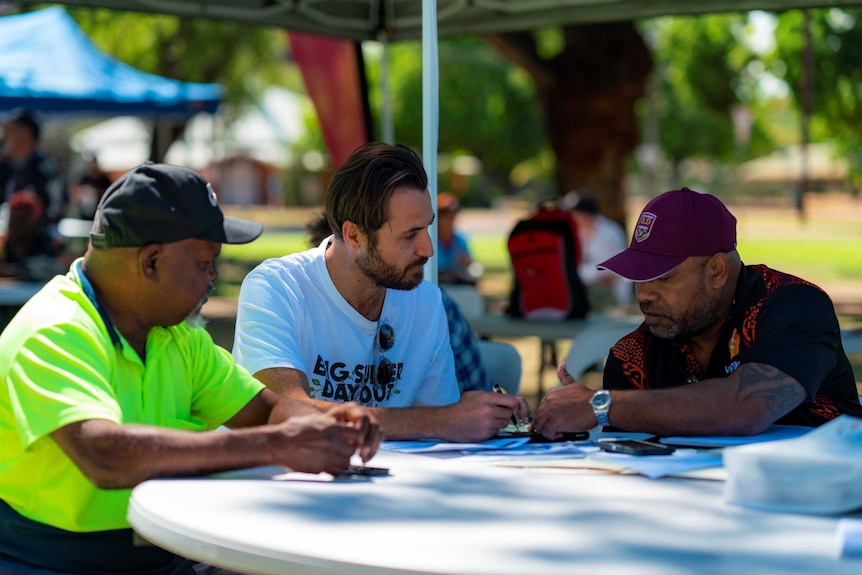 Three men sit around a table in a park in Kununurra.