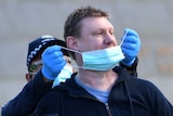 Victoria Police put a mask on an anti-lockdown protester at Melbourne's Shrine of Remembrance.