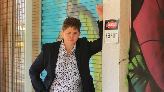 A woman stands with her arm leaning against a post near a closed roller door.