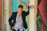 A woman stands with her arm leaning against a post near a closed roller door.