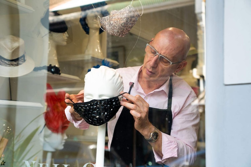 a tailor at a window shop putting a mask over a mannequin head