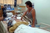 Ben French's mother strokes her son's arm while he is in a coma in hospital.