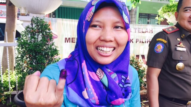 A woman in Jakarta shows off her ink-stained finger after voting.