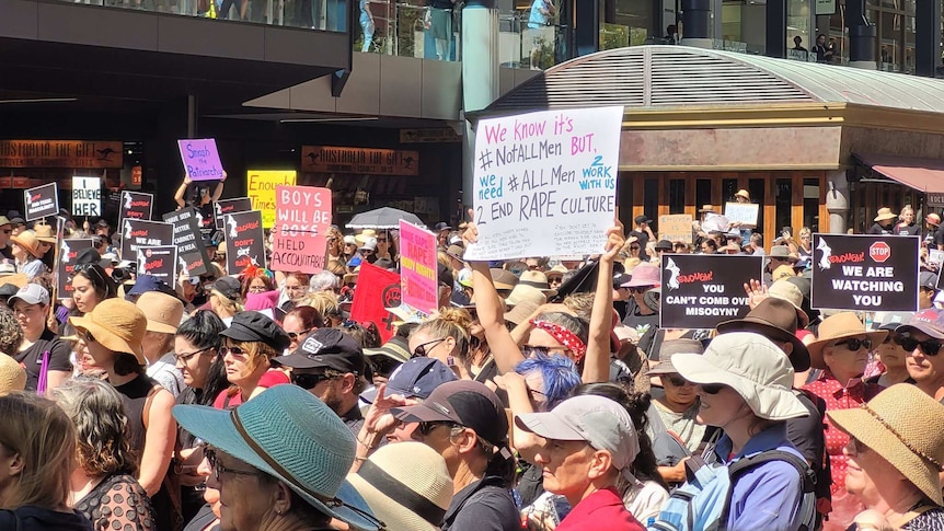 A woman holds a sign at the international Women's day march in Perth reading "we need all men to work to end rape culture'.