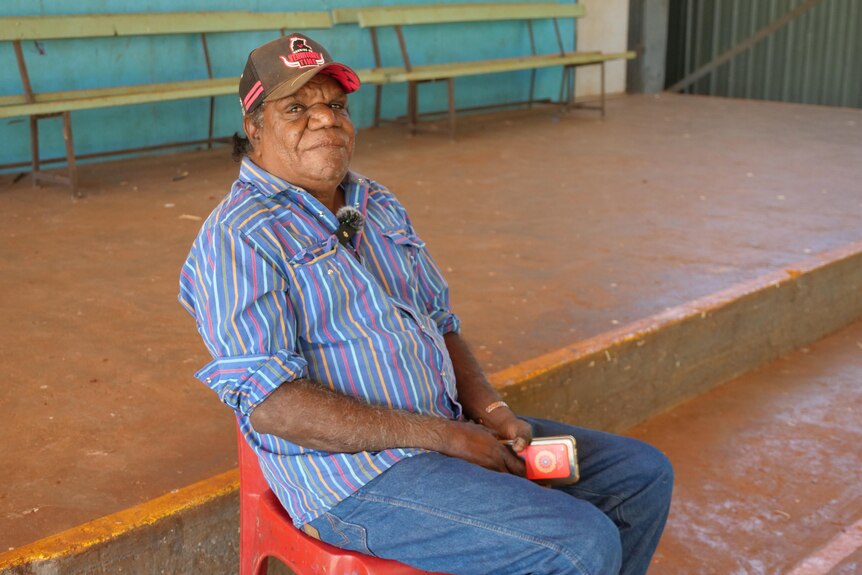 An Aboriginal man wearing an Essendon football club cap and stripey shirt.
