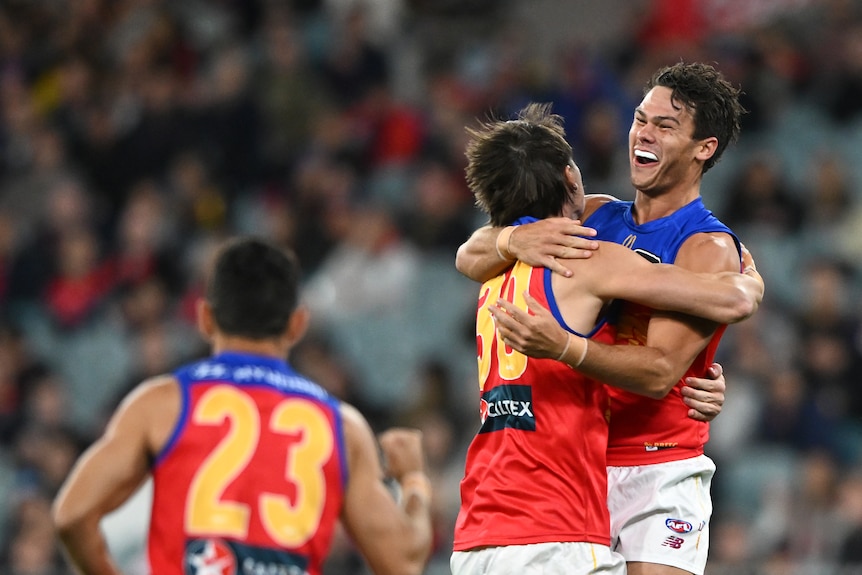 Two AFL teammates embrace after a goal is kicked, with another running towards them to join