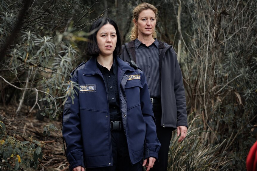 Two policewomen, one in uniform, standing in the bush, looking shocked in a still taken from TV show Deadloch.