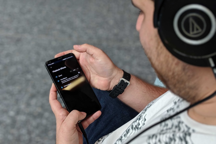 A man with headphones on holding a phone with "playback effects" options he's selected x3 speed.