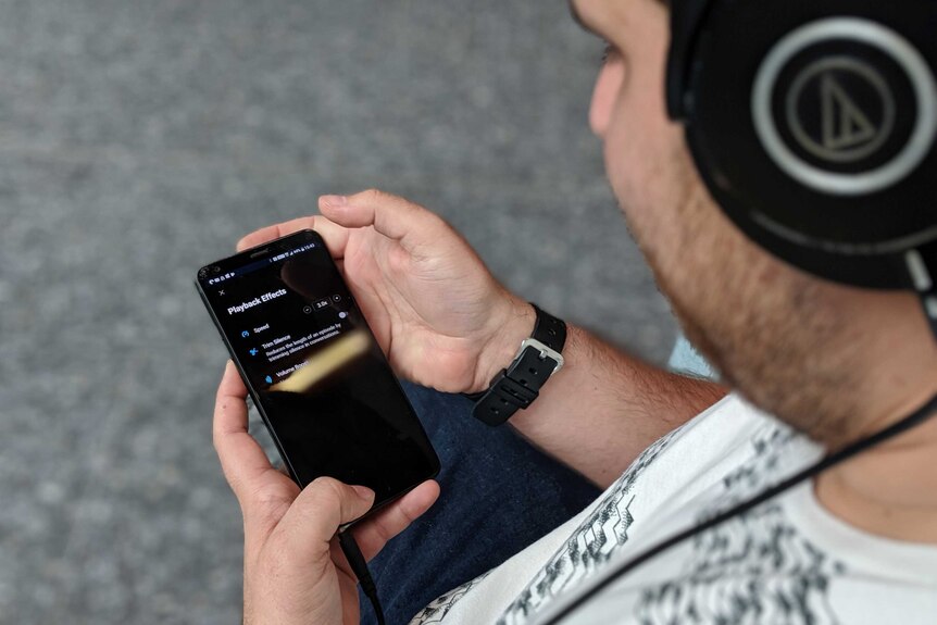 A man with headphones on holding a phone with "playback effects" options he's selected x3 speed.