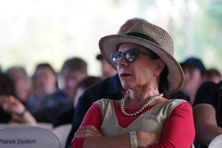 Linda Burney, arms crossed in front of her, wearing a straw hat, glasses and matching jewellery.