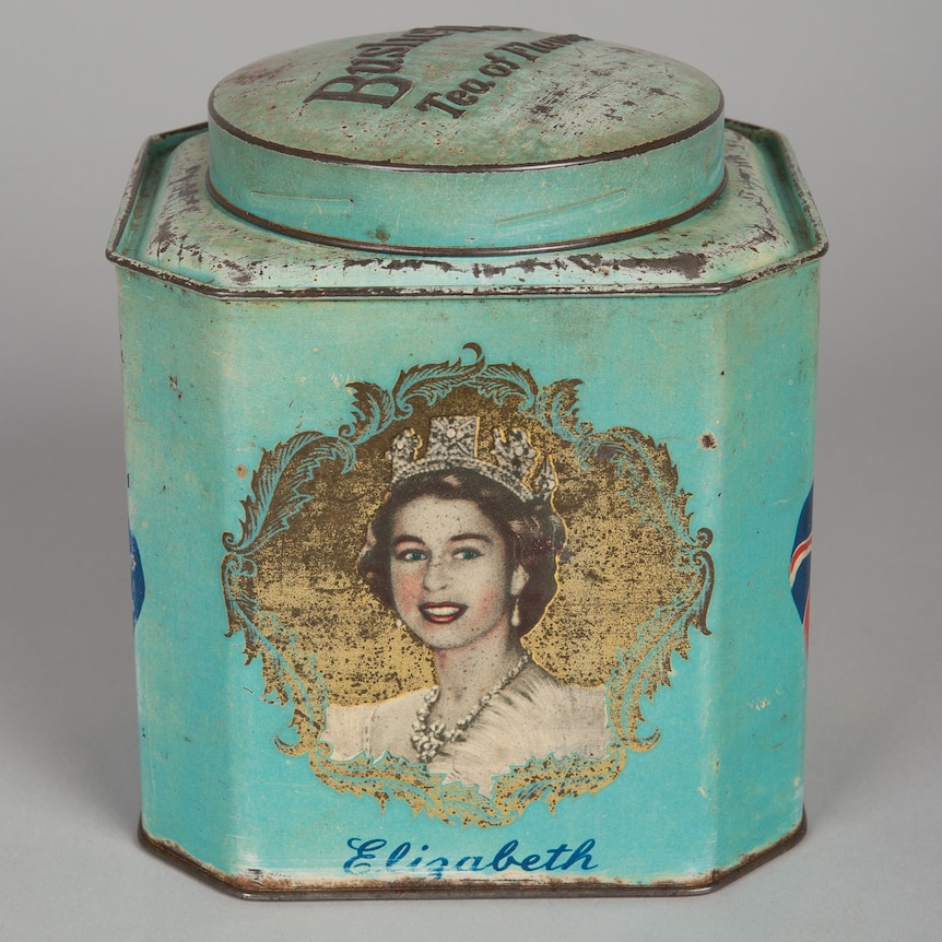 You view a rusted Bushells tea tin that is coloured in a fading aqua, carrying a portrait of a young Queen Elizabeth.