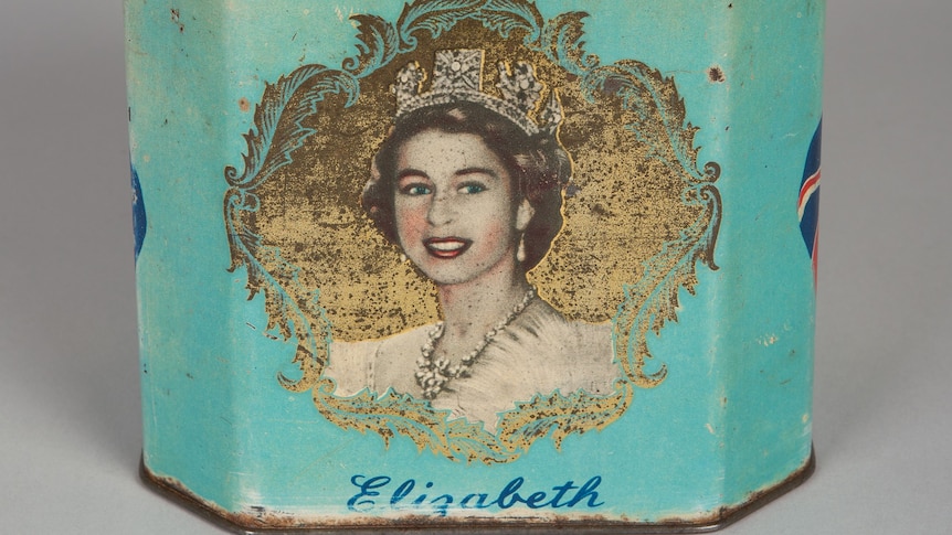 You view a rusted Bushells tea tin that is coloured in a fading aqua, carrying a portrait of a young Queen Elizabeth.