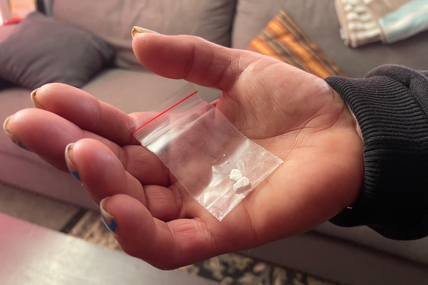 Small rocks of heroin inside a plastic bag held by an unidentifiable white hand.
