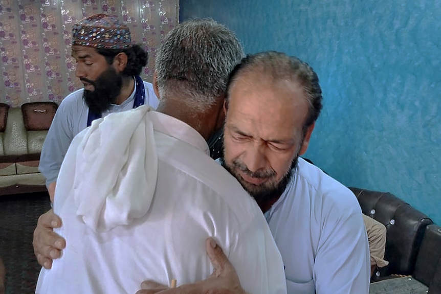 Two middle eastern men embrace as one cries into the other's shoulder. 