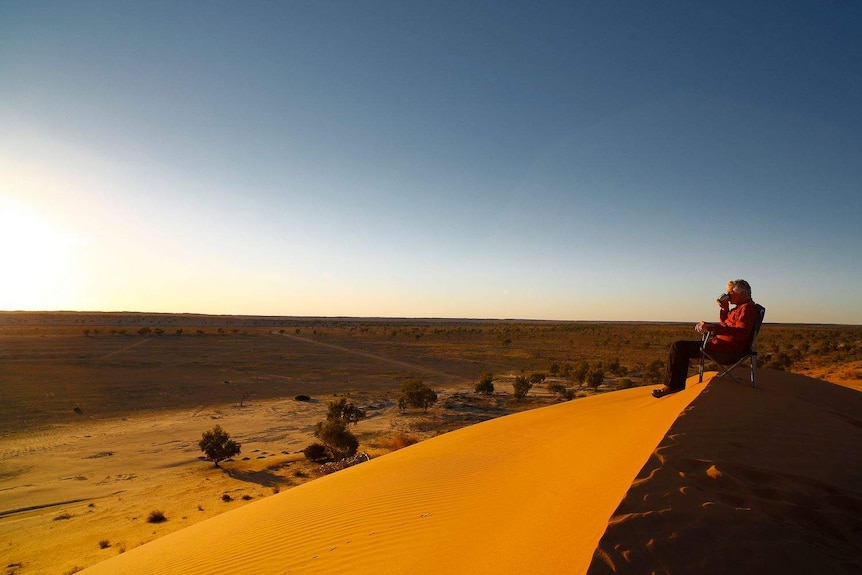 A man sitting on top of a sand hill.