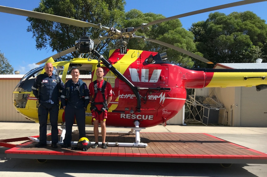 Three men stand in front of a rescue helicopter