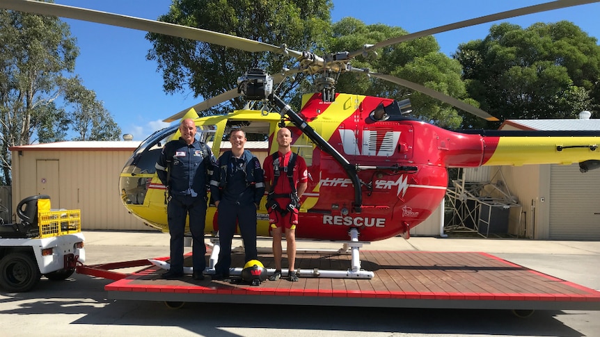 Three men stand in front of a rescue helicopter